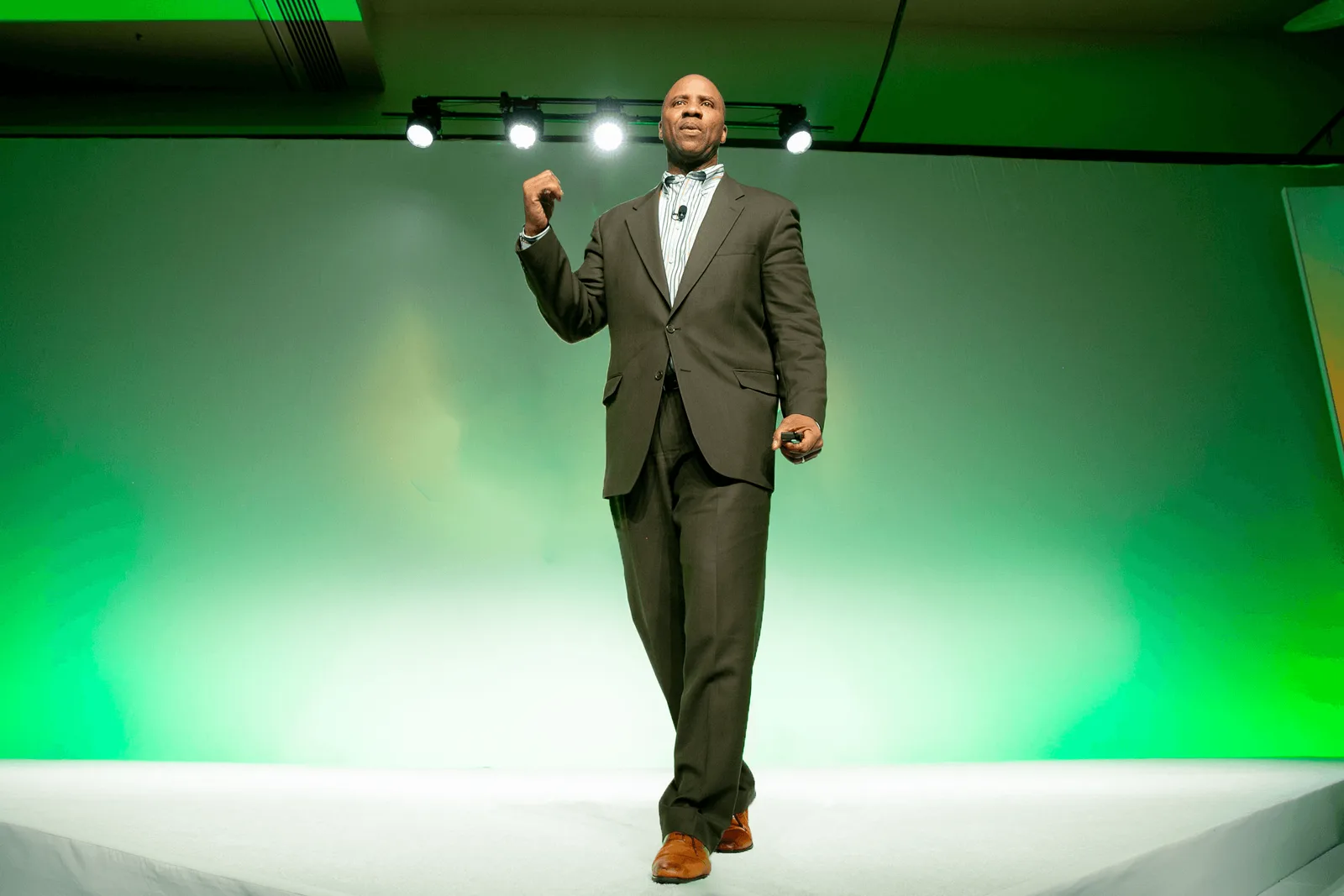 Rutherford Pascal walking a stage mid-talk, lit against a green backdrop